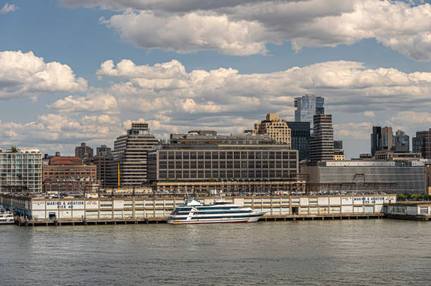 New York, NY, USA - August 1, 2023: Hudson River shoreline view between W. Houston and Spring streets under blue cloudscape. Marine and aviation pier 40 in front and docked City Cruises boat