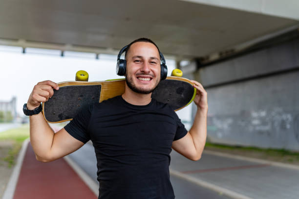 istock Man holding skateboard smiling with headphones 2154009358