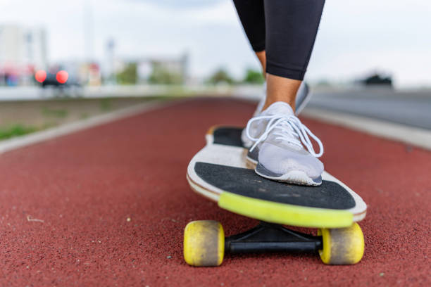 Silhouette close up photo of skater legs is standing on long board on mountain road against sunset sky