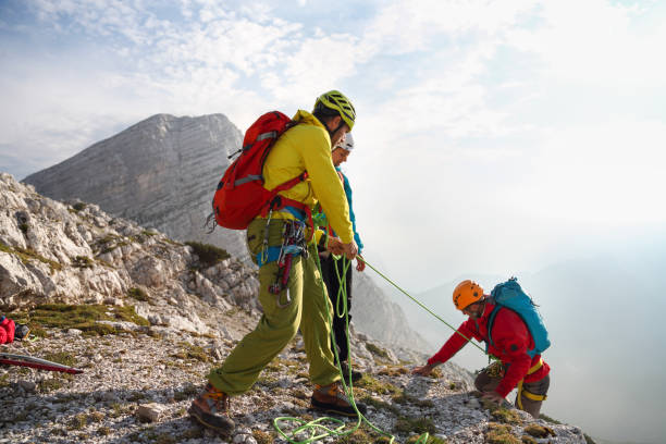 Mountain guide in full equipement helping others to the top of the mountain. Ropes, shoes, helmets, backpacks...