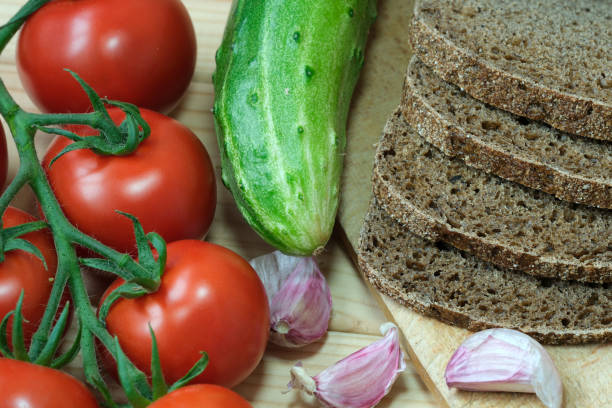 A pile of bread sits next to a pile of tomatoes and a cucumber.