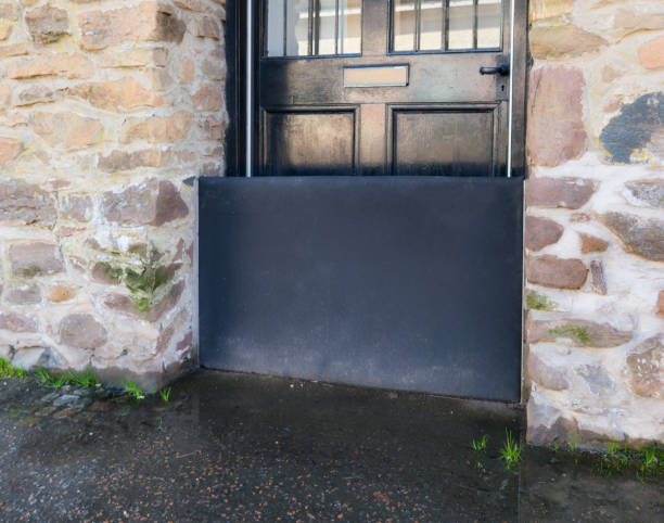 Close-up of a flood barrier protecting a front door from water ingress, with standing water on the pavement in front.