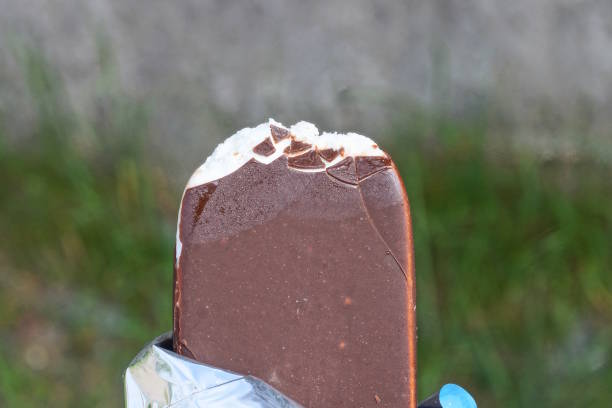 a piece of white ice cream in brown chocolate on a green background on the street