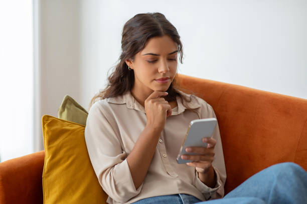 istock Thoughtful young woman touching chin while reading message on smartphone at home 2154026313
