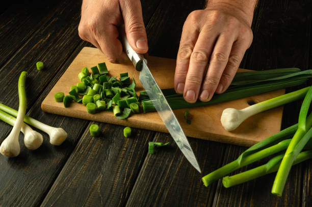 Slicing fresh garlic with a knife in the hands of a chef on a cutting board. Low key concept of preparing vegetable salad. Advertising space