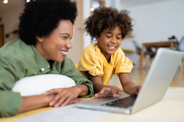 istock Smiling mother and daughter using laptop while relaxing at home 2154040036