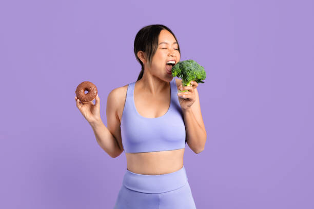 Asian woman in sportswear bites broccoli and holding donut