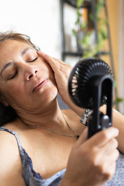 istock woman sweating and using a hand-held electric fan.summer heat wave.vertical image. 2154042424