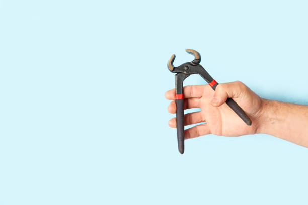istock Man hand holding pincers on a light blue background with copy space 2154043197
