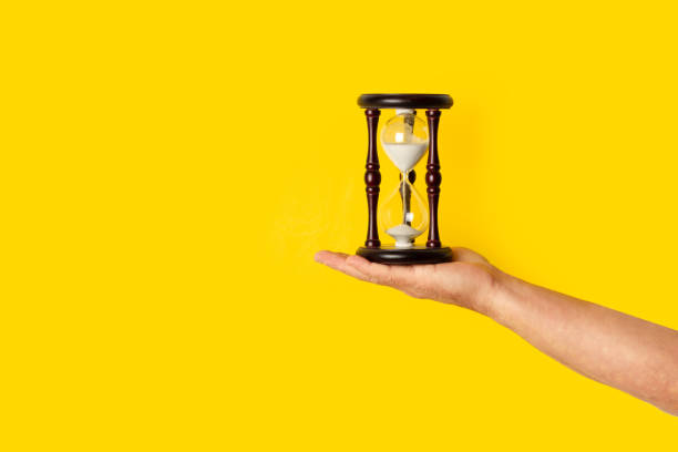 istock Man hand holding a hourglass on a yellow background with copy space 2154043217