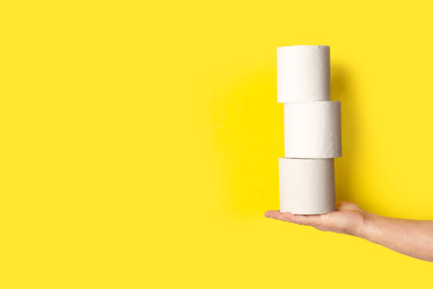 istock Man hand holding three toilet paper rolls on a yellow background with copy space 2154043219