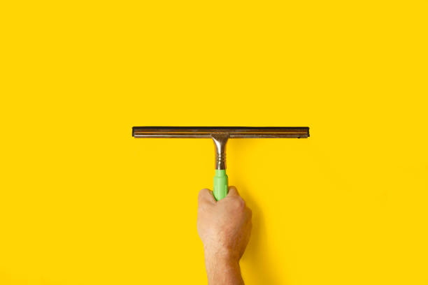 Man's hand holding a glass cleaner on a yellow background with copy space