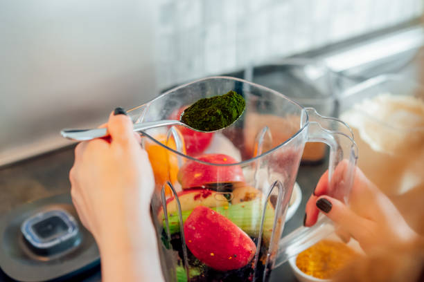 istock Close up woman adding spirulina or chlorella powder during making smoothie on the kitchen. Superfood supplement. Healthy detox vegan diet. Healthy dieting eating, weight loss program. Selective focus 2154044267