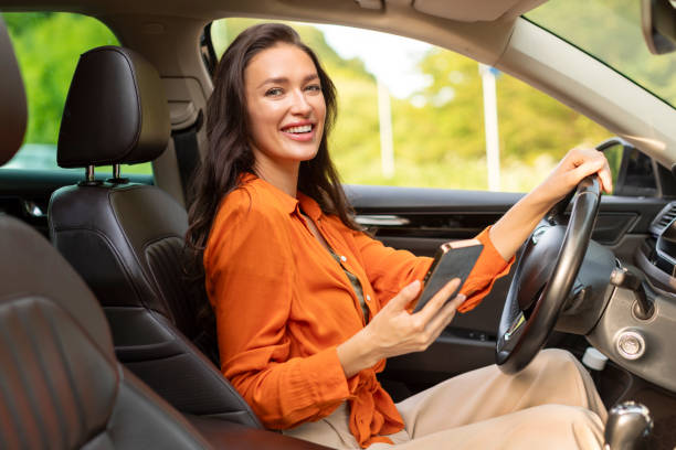istock Car navigation app. Happy woman driver using cellphone sitting in automobile and smiling, websurfing road and using gps navigator 2154045680