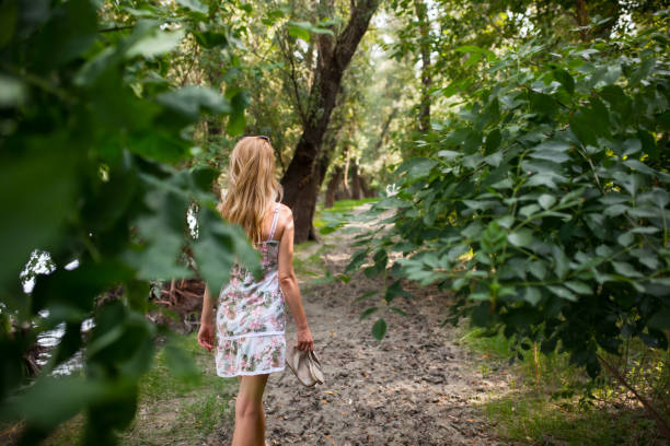istock A lone woman walks down a lush forest path, holding her shoes in one hand, surrounded by vibrant greenery during a peaceful summer day. 2154046366