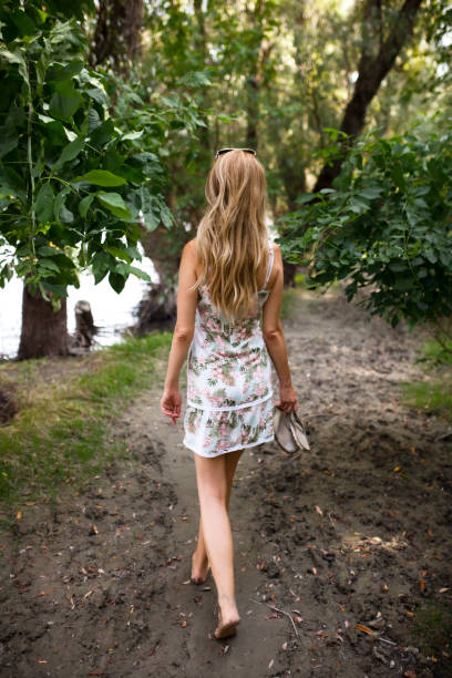 istock A serene image capturing a young woman from behind as she walks down a peaceful, muddy path among vibrant green trees and near a river. 2154046461