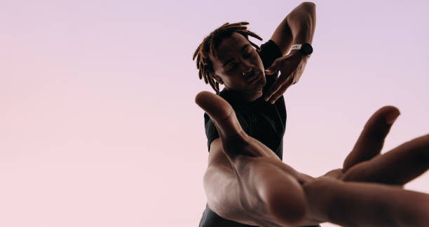 Expressive gen z male dancing to music with wireless earbuds in studio Young man with dreadlocks dances energetically to the rhythm of music in a studio. Expressive and artistic, he moves gracefully with eyes closed, hands expressing the beat. Wearing a smartwatch and wireless earbuds, he listens to his playlist. african rhythm stock pictures, royalty-free photos & images