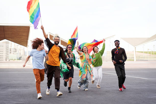 istock People celebrating the pride day, holding rainbow flags while running excited and looking at camera. 2154050152