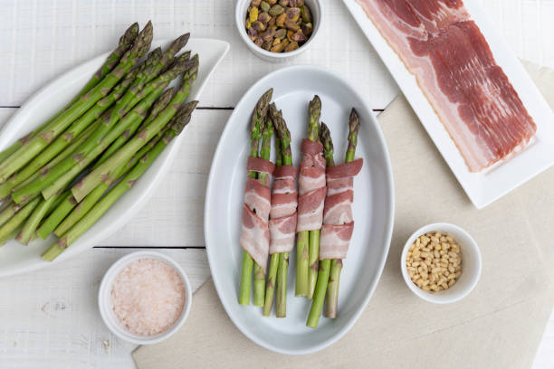 istock Crisp Green Asparagus shown on baking tray, ready for oven. Framed by plate with bacon and other ingredients 2154050972
