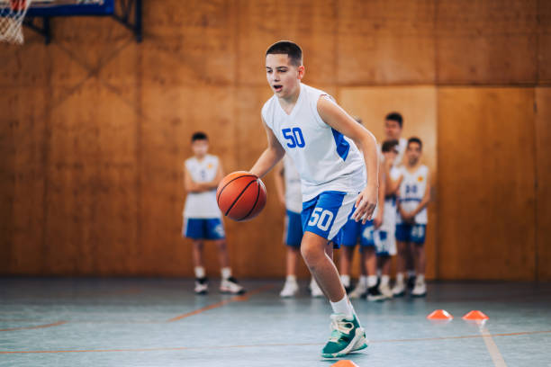 Junior basketball player dribbling a ball at indoor court on training Full length of a junior basketball player in action dribbling a ball on training at court. A young athlete in motion practicing basketball while dribbling a ball on court. A sporty kid with basketball secondary school activities stock pictures, royalty-free photos & images