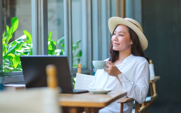 istock Portrait image of a young woman with hat drinking coffee while working on laptop computer in cafe 2154078123