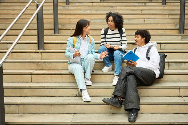 istock Three young students sitting on steps, one of them reading a book 2154079850