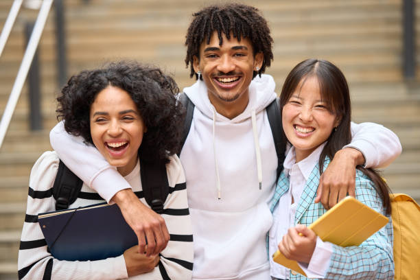 istock Three young students are smiling and hugging each other while holding books and looking at camera 2154079868