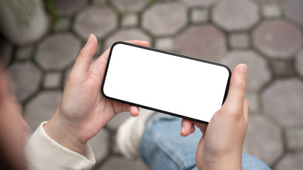 istock A woman holding a smartphone with a white-screen in a horizontal position while sitting outdoors. 2154087216