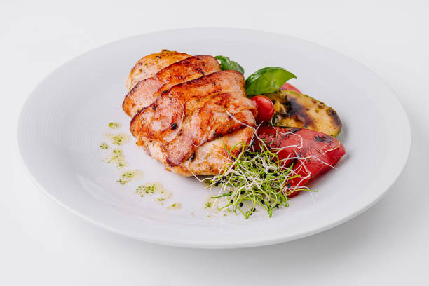 Juicy grilled chicken breast with grilled vegetables, garnished with microgreens on a white plate