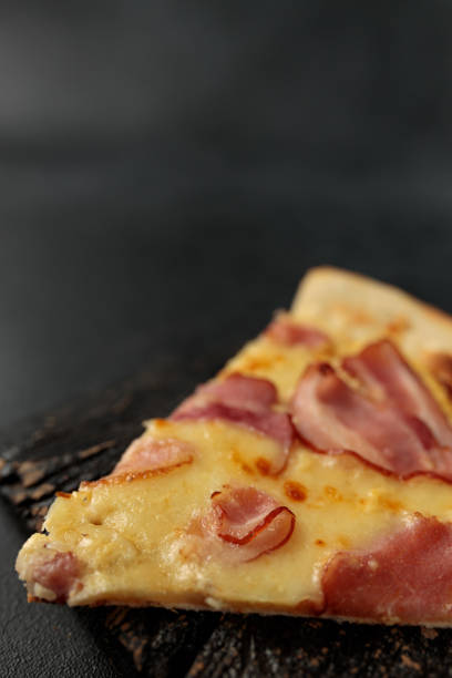 Piece of Pizza Carbonara on a black cutting board. Black background. Space for text