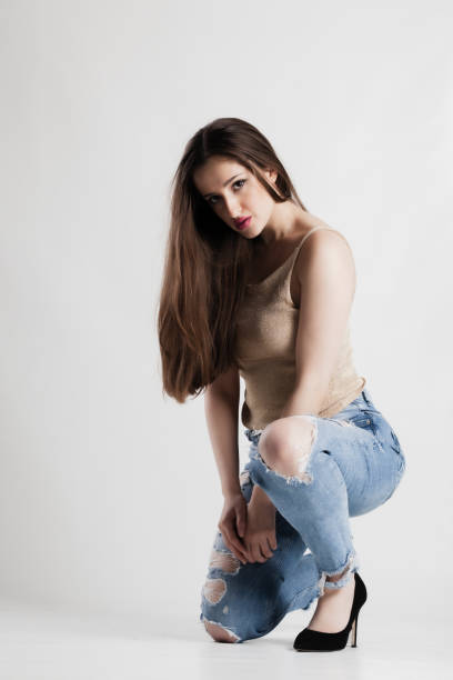 istock Young woman in distressed jeans and gold top posing in a studio 2154099472