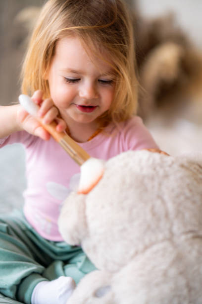 Close-up of cute little girl playing whit make-up brush and her teddy bear at home