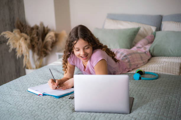istock Cheerful girl doing homework on a bed 2154108880