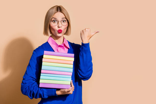 istock Portrait of clever impressed lady pouted lips hold pile stack book indicate finger empty space isolated on beige color background 2154109164