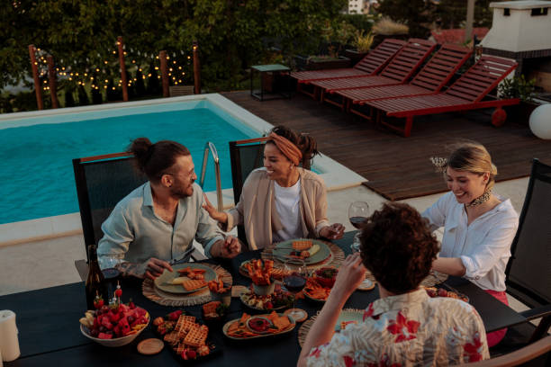 istock Four friends having dinner and laughing by a poolside 2154111306