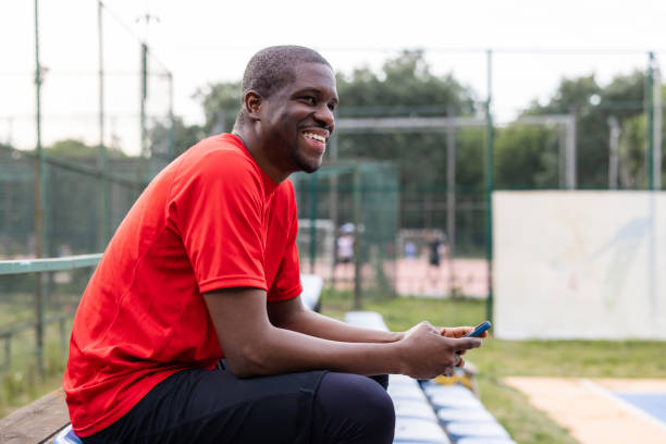 istock African American man sitting on bleachers, using smart phone and smiling 2154111580