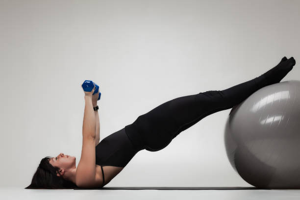 istock Young woman exercising with dumbbell and stability ball in a studio 2154112994