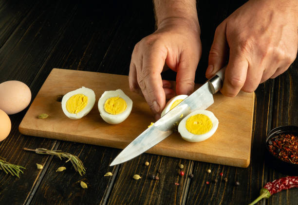 istock Slicing boiled eggs on the kitchen table. A knife in the hand of a chef cuts an egg for preparing breakfast at the cook room 2154116854