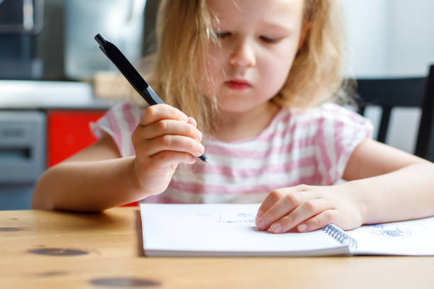 istock portrait of a girl sitting at the table in the kitchen and drawing in a notebook. 2154118708