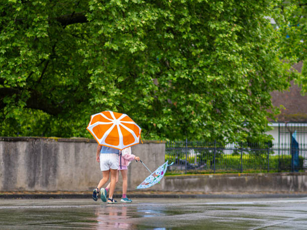 Couple in yellow raincoats kissing under the umbrella during rainy day at the park. Copy space.