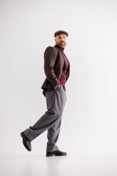 istock Stylish man in plaid flat cap, jacket and pants walking on gray background 2154131948