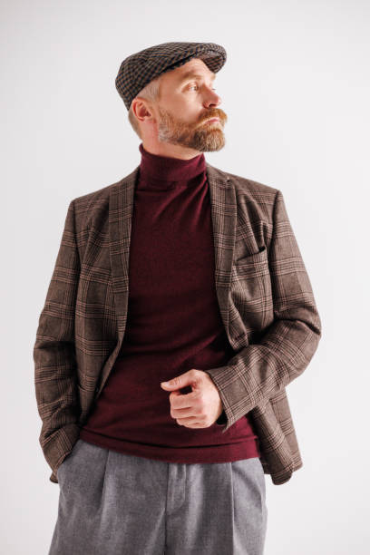 Stylish man in plaid jacket, flat cap and turtleneck posing cut out on gray background