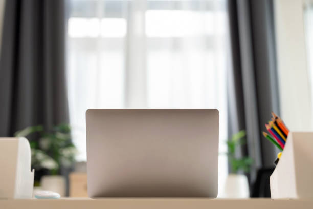 A laptop on a table in a cozy living room at home, with sunlight streaming through the window in the background. The scene exudes a modern and comfortable atmosphere, perfect for remote work or leisurely browsing.