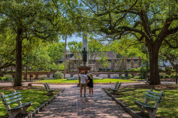 Charleston, South Carolina - May 7, 2024:  Visitors looking at George Washington statue at the Washington Square Park in the heart of Charleston on a sunny day under heavy shade of mature Southern Live Oak trees with resurrection fern.  HDR encoded.