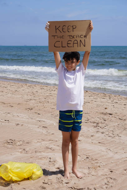 istock boy picking up plastic from the seashore and holding a banner that reads 