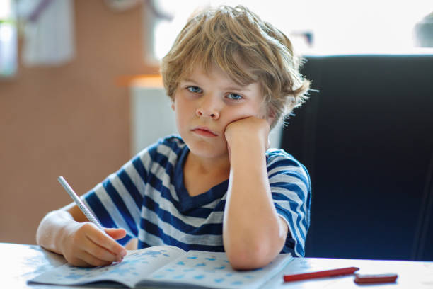 istock Portrait of tired upset boy doing homework in kitchen at home. Elementary school studing writing and learning. Sad and angry child. 2154163011