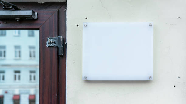 istock Blank white signboard on wall with screws, mockup for logo or text. Clear signage on textured wall beside wooden door frame 2154166778