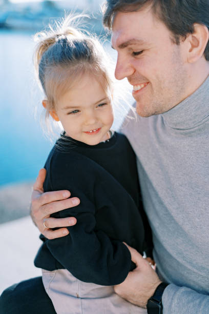 istock Smiling dad looking at little girl sitting on his lap while hugging her 2154166934