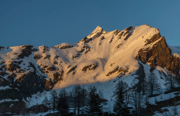 Sunny snowy evening on Simplonpass with blue sky and orange lights