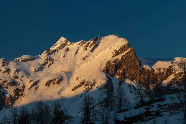 istock Sunny snowy evening on Simplonpass with blue sky and orange lights 2154174139